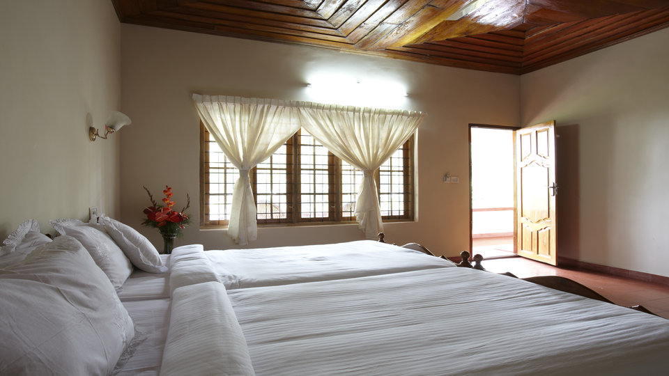 Bright bedroom with twin beds, sheer curtains and a door opening onto the balcony in the morning light